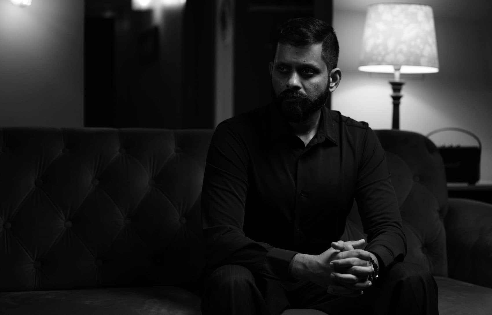 Shashank on a dark sofa, the seat beside him empty.